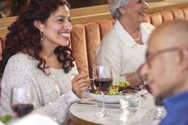 No3 at Nightingale Place Two women sit at a restaurant table enjoying a meal and conversation. One holds a glass of red wine. A man is in the foreground, partially facing away, looking at a menu.