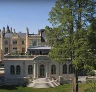Large historic mansion with Gothic-style features, multiple chimneys, arched windows, and a landscaped garden with tall trees and manicured lawns.