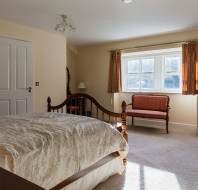 A cozy bedroom with a wooden bed, an armoire, a window with curtains, and a small upholstered bench.