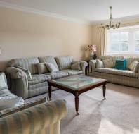 A living room with striped sofas, a glass-top coffee table, decorative lamps, and a window with curtains.