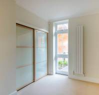 Minimalist room with beige carpet, sliding glass closet doors on the left, a tall window, and a white wall-mounted radiator on the right.