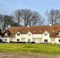 Row of white houses with brown roofs, set in front of leafless trees, facing a circular lawn area.