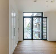 Empty modern room with wooden flooring, large window, and a view of neighboring buildings.