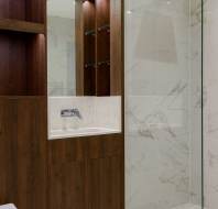 Modern bathroom with marble tiles, glass shower enclosure, and a dark wood vanity with sink and mirror.