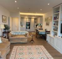 Cozy living room and open kitchen with a dining area, featuring sofas, a patterned rug, bookshelves, and framed art on the walls.