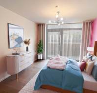 A modern bedroom features a bed with blue bedding, a pink accent wall, a dresser with decor, large windows with curtains, and a ceiling light fixture.