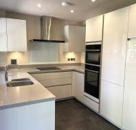 Modern kitchen with white cabinets, built-in oven and microwave, induction cooktop, stainless steel extractor hood, and a sink with a sleek faucet on a gray countertop.