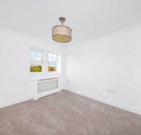 Empty room with white walls, beige carpet, a window with a radiator cover beneath, and a ceiling light fixture.