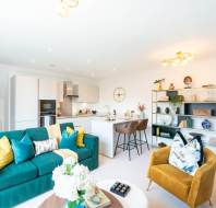 Bright, modern open-plan living space with a green sofa, mustard armchair, kitchen island with bar stools, dining area, and decorative shelving.