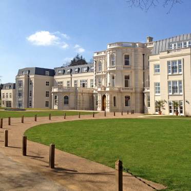 Large cream-colored historic building with multiple windows, ornate architectural details, and a manicured lawn under a clear blue sky.