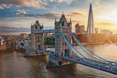 Tower Bridge spans the River Thames in London at sunset, with the Shard skyscraper and nearby buildings visible in the background.