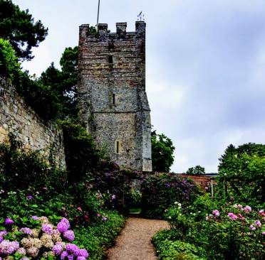 Greys Court A stone tower stands amidst a garden with colorful hydrangeas under a cloudy sky.