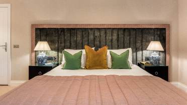 A neatly made bed with a wooden headboard, green and yellow accent pillows, matching bedside tables with lamps, and books on each table.