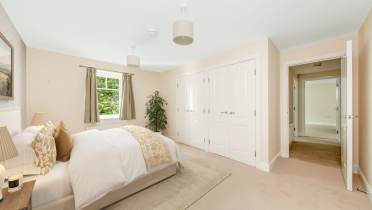 Bright, neutral-toned bedroom with a double bed, bedside tables, two white closets, a window with green curtains, and an open door leading to a hallway.