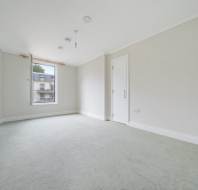 Empty room with light-colored carpet, white walls, a single open window, ceiling lights, and a closed door.