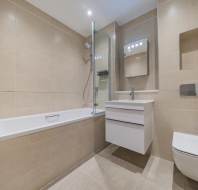 Modern bathroom with beige tiles, a bathtub with a glass shower screen, a wall-mounted sink with cabinet, toilet, and a large mirrored cabinet.