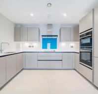 Modern kitchen with light gray cabinets, white countertops, built-in oven and microwave, induction cooktop, and a blue backsplash under a stainless steel range hood.