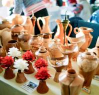 A display of various handcrafted wooden vases and vessels with price tags, alongside artificial red and white flowers on a table.