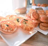 Two white plates on a wooden table, one with small vegetable quiches and the other with stacked mini pies, displayed in natural light.