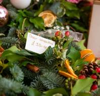 A display of festive door wreaths decorated with foliage, dried orange slices, pinecones, and berries, with a handwritten sign reading "Door Wreaths £35.00".
