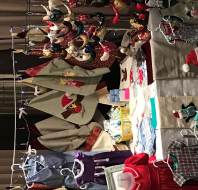 A display table at a craft fair features handmade children's clothes, holiday-themed tote bags, and various decorative ornaments, including fabric animals and festive designs.