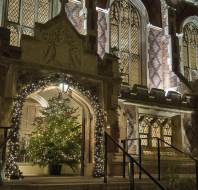 A decorated Christmas tree with lights stands under an arched entrance of a building with illuminated windows at night.