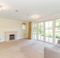 Spacious living room with beige carpet, fireplace, gray sofa, and large windows with yellow curtains overlooking a garden patio.