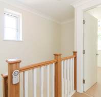 Small upstairs landing with a wooden railing, cream-colored walls, a closed window, and an open door leading into a bright room.