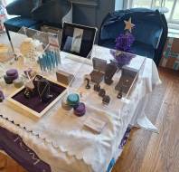 A display table with jewelry, cosmetics, and decorative items set up indoors, featuring necklaces, rings, and holiday-themed decor.