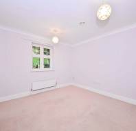 Empty room with light-colored carpet, white walls, and two ceiling lights. A window is on one wall, and a white door is on another.