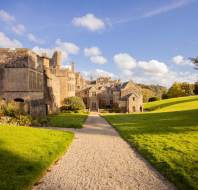 A historic stone mansion surrounded by lush green lawns, set under a clear blue sky.