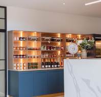 A modern interior featuring a marble counter and a shelved bar area with various bottles and jars on display.