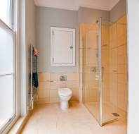 Modern bathroom with beige tile flooring, a glass shower enclosure, a wall-mounted toilet, a towel rack, and a frosted window allowing natural light in.