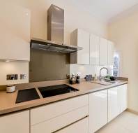 Modern kitchen with glossy white cabinets, beige countertops, a black cooktop, and stainless steel range hood; jars and kitchen items are neatly arranged on the counter.