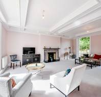 Spacious living room with large windows, light-colored walls and carpet, a fireplace, sofas, armchairs, coffee tables, TV, and decorative items.