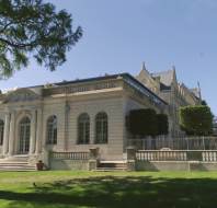 Large, elegant stone building with arched windows, ornate detailing, and manicured lawn under a clear blue sky.