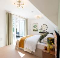 A bright bedroom with a double bed, green and yellow accents, modern lighting, wall art, and glass doors opening to a balcony.