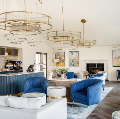 Modern lounge area with blue and white furniture, circular chandeliers, art on walls, and a bar with a coffee machine.