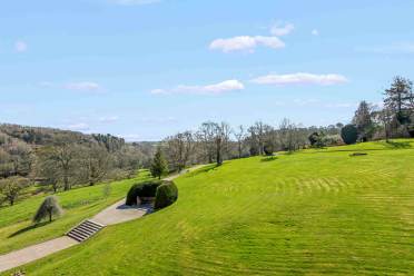 Grounds A large, well-kept green lawn with scattered trees, a stone staircase, and a paved path under a clear blue sky with a few clouds.