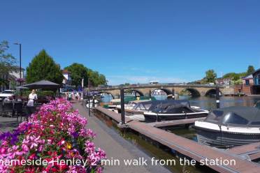 A riverside walkway in Henley with boats docked, colorful flowers in the foreground, and a stone bridge in the background; text reads "Thameside Henley 2 min walk from the station.